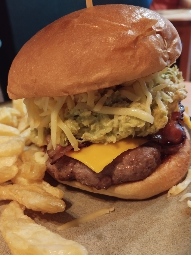 Carta de Restaurantes en Coruña, Cheesy Burger, The tropical burger: carne, cheddar, gouda rallado, bacon bañado en sirope estilo americano, salsa dijonnaise, pollo deshilachado, guacamole y salsa tropical